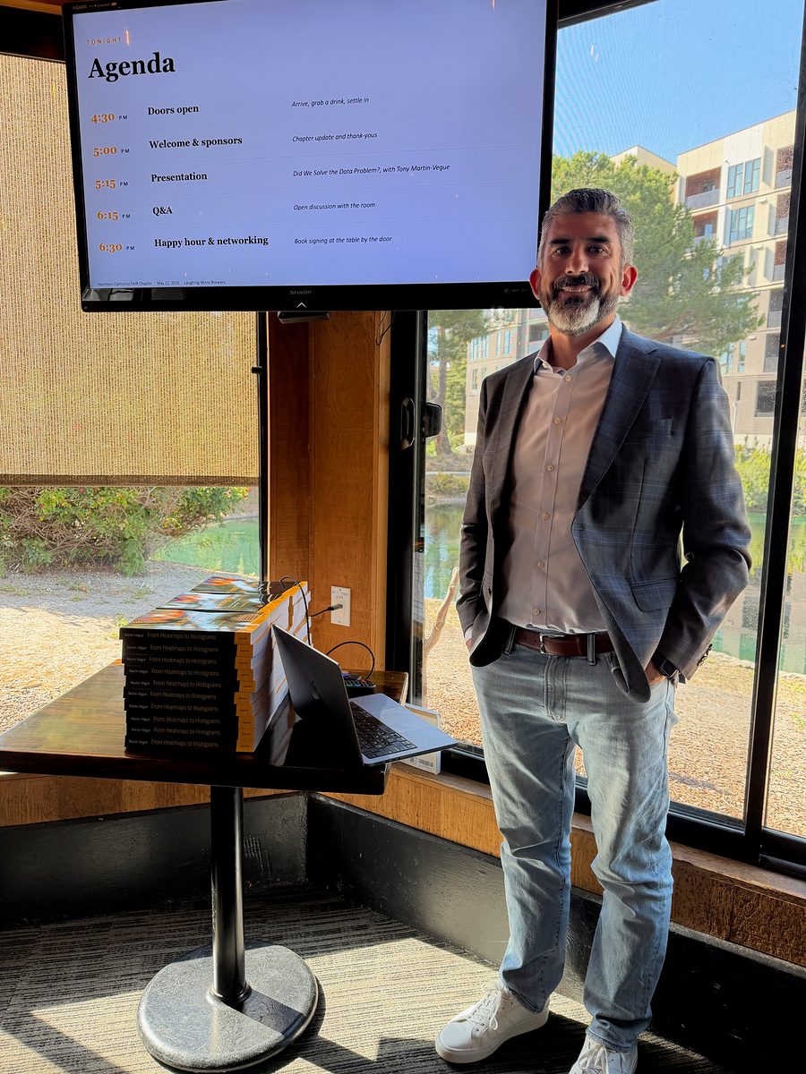 Tony Martin-Vegue beside an agenda screen for his talk, with a stack of his book, From Heatmaps to Histograms, on a table